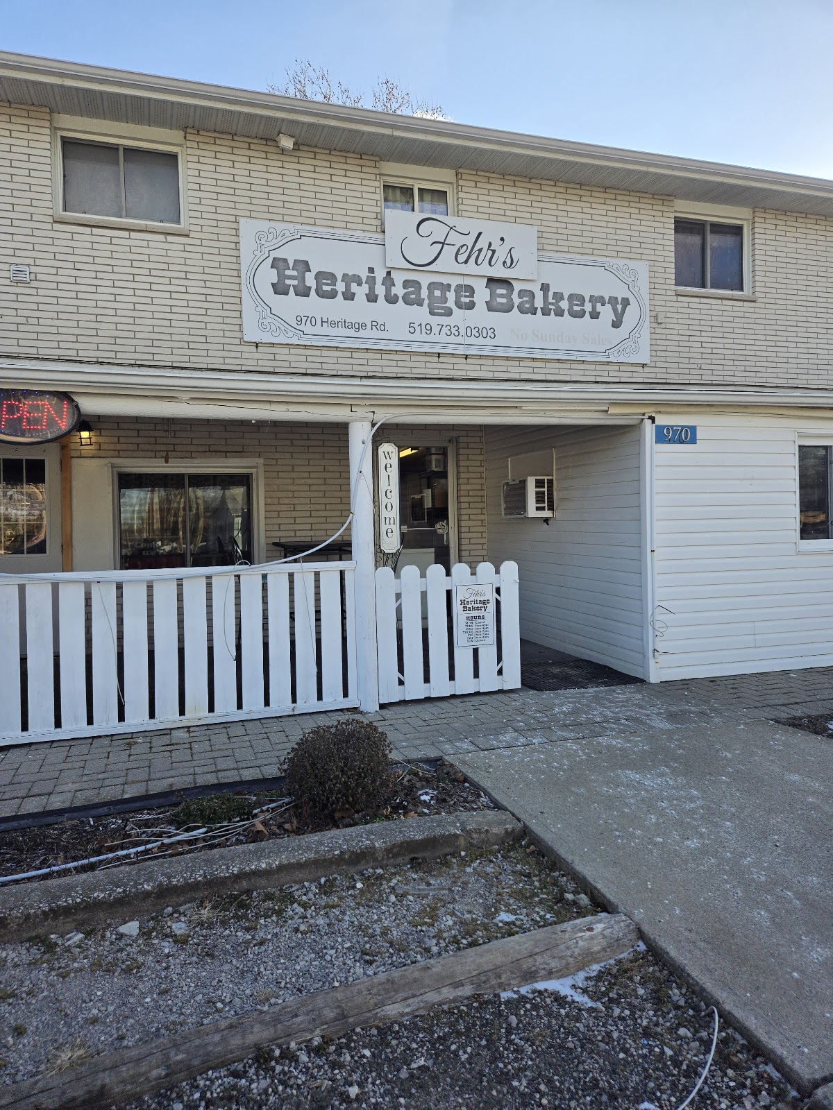 Exterior of Fehr's Heritage Bakery, a white building with a hand-painted sign, white picket fence, and steps leading to the entrance
