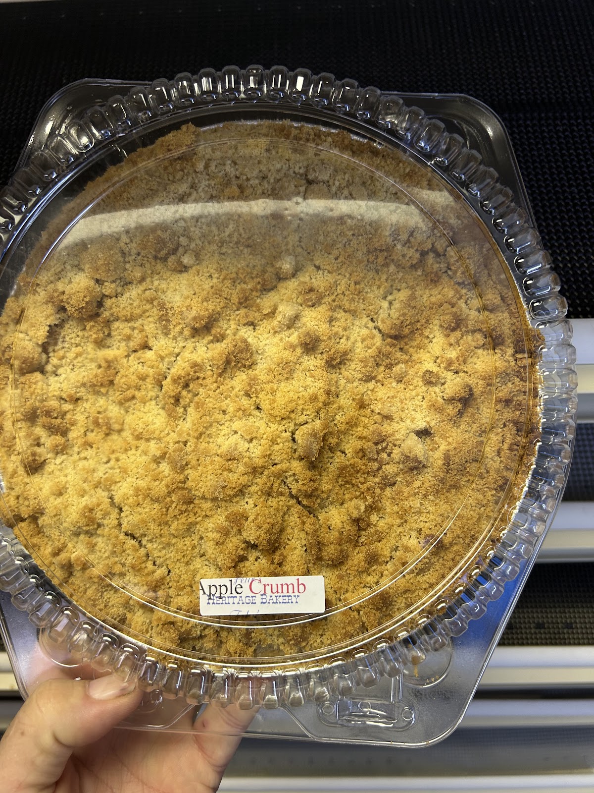 A fresh apple crumb pie with golden streusel topping held up in front of the bakery shelves